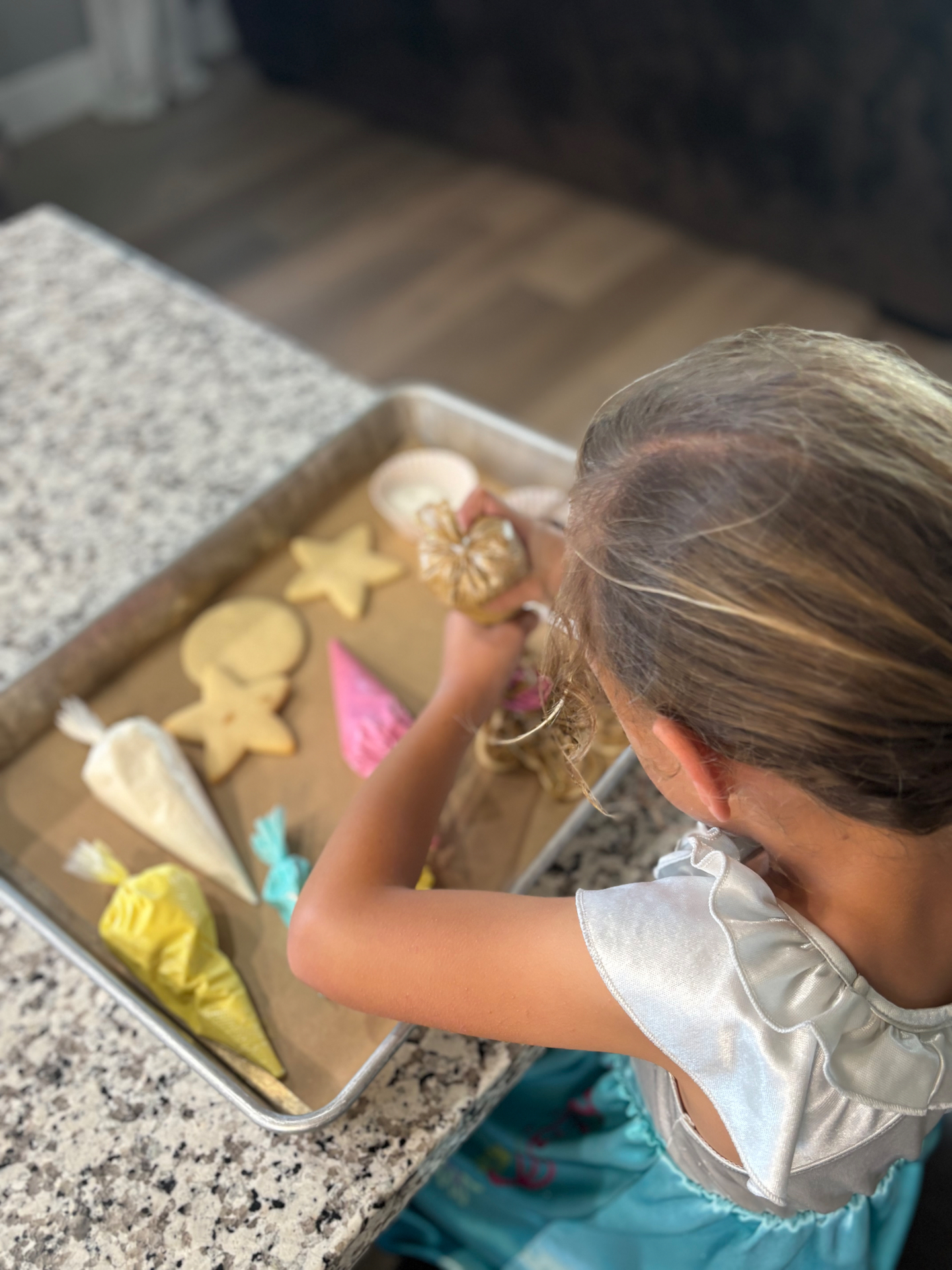 Overhead view of a child decorating sugar cookies with piping bags of buttercream